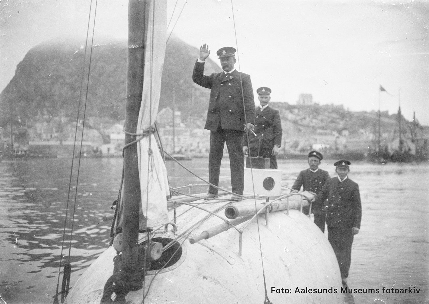 URÆD vessel with uniformed crew standing on deck in Ålesund, with the town and mountains in the background.