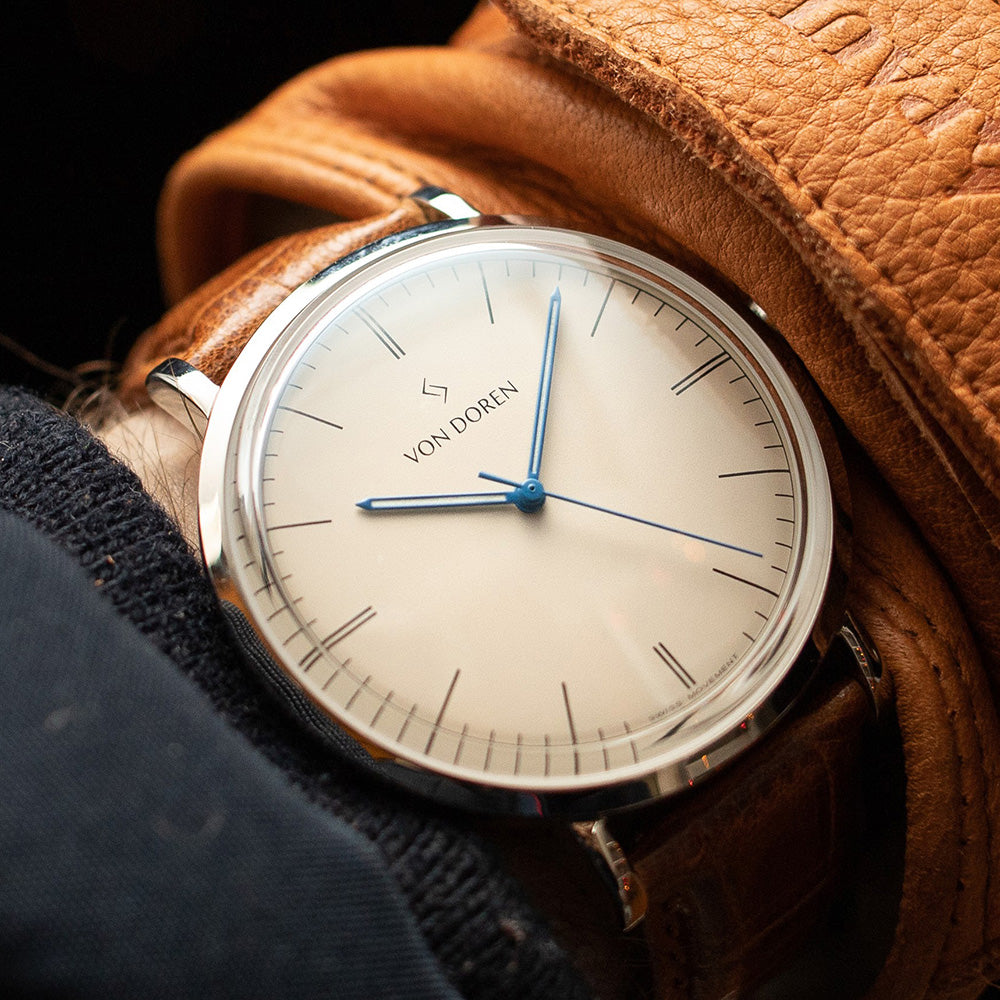 Von Doren klokke. Modellen Aksla Mark II,i fargen Antique White. Klokken er på en arm med en brun skinnhanske.