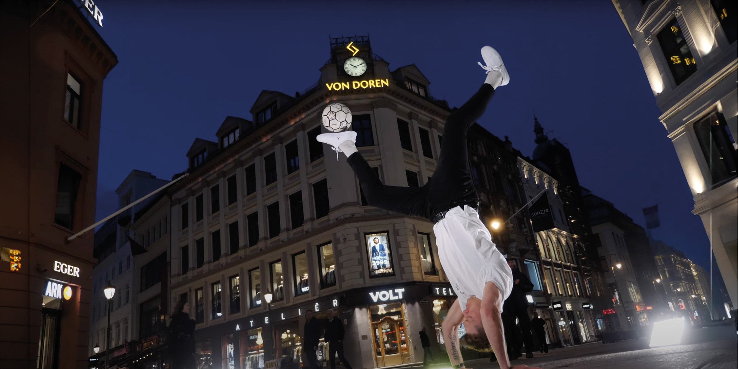 Tobias Becs doing a freestyle handstand with a football in front of the Von Doren sign.