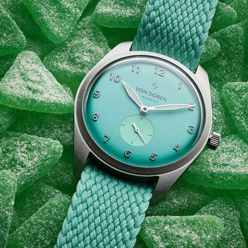 Klokke i mintgrønn farge liggende oppå grønne gele godterier