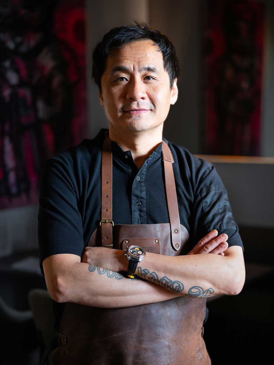 Chef wearing a Von Doren watch, arms crossed in a restaurant setting.