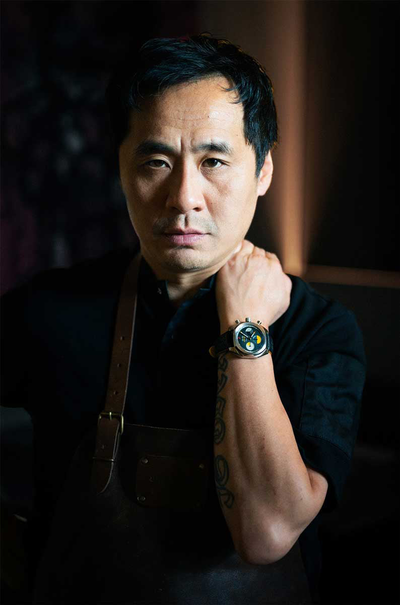 Chef showcasing a Von Doren watch, hand raised to his neck.