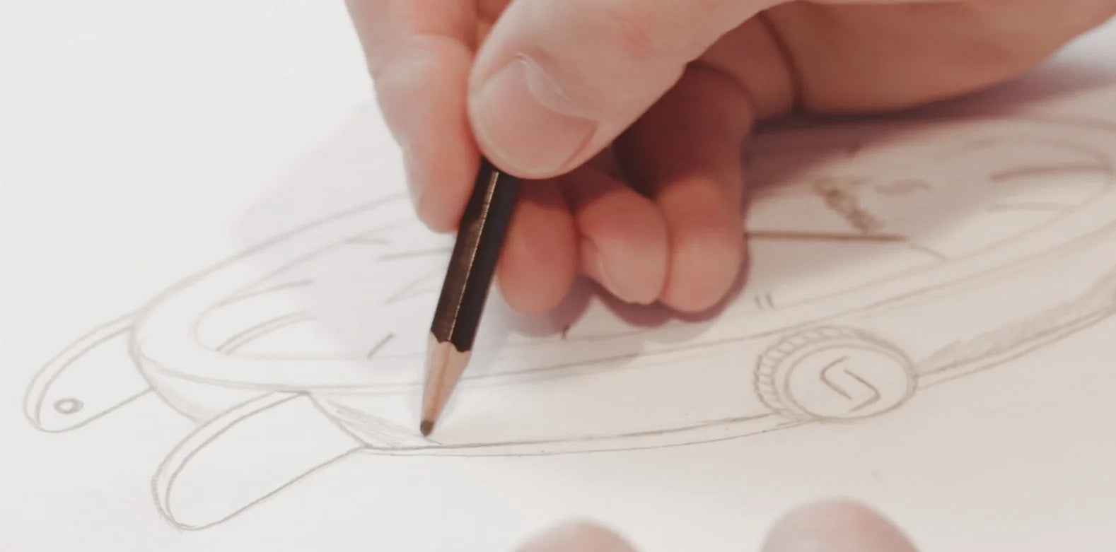 Close-up of a hand sketching a watch design with a pencil.